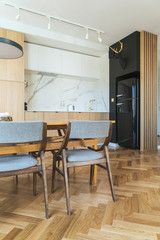 Stylish and cozy scandinavian dining room and kitchen with design family table, chairs and lamp. White walls and brown wooden parquet.