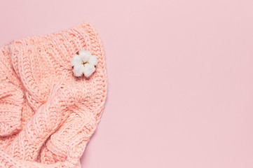 Female pink knitted sweater pullover and flower of cotton on pastel pink background top view flat lay. Fashion Lady Clothes Jumper Autumn winter clothes fashion look Delicate cotton flowers Lifestyle