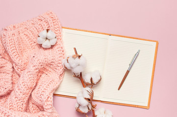Female pink knitted sweater, cotton, open blank notebook, pen on pastel pink background top view flat lay. Lady winter Clothes. Cotton flowers. Lifestyle gentle female background