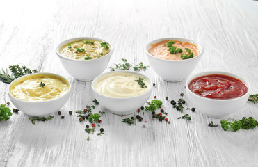 Different tasty sauces in bowls with spices on white wooden table