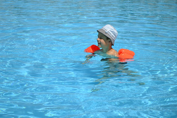 A boy 7 years old swiming and playing in a pool with resque rings