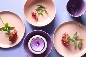 Tableware, candle and flowers on violet background