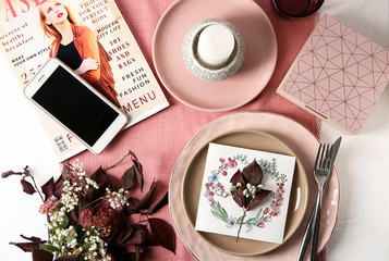 Flat lay composition with tableware, mobile phone, floral decor and magazine on color background