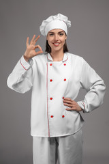 Young female chef on grey background