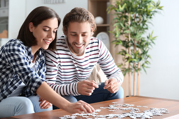 Young couple doing jigsaw puzzle at home - obrazy, fototapety, plakaty