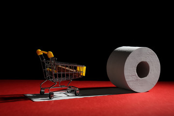 Roll of toilet paper and small shopping cart on table against dark background