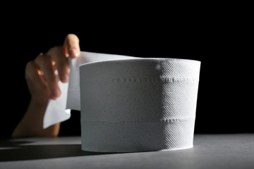 Female hand and roll of toilet paper on dark background