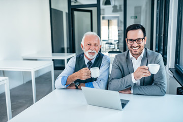 Portrait of a senior business man and younger colleague drinking coffee in the office.