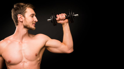 Fototapeta na wymiar Confident young man shirtless portrait training with dumb-bell against black background.