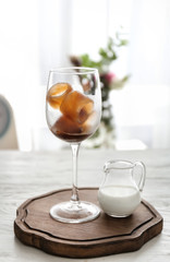 Glass with coffee ice and jug of milk on table
