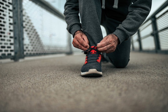 Close-up image of senior man preparing for a run outdoors. Tying shoelaces.