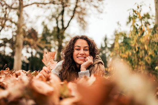 Low angle image of curly brunette relaxing in autumn park.