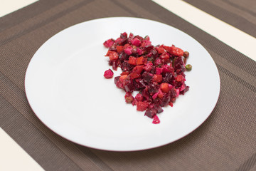 Vinaigrette salad of beet, carrots, peas, onions, potatoes on a white plate.