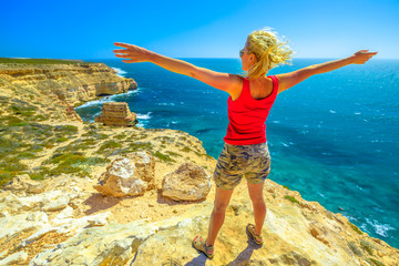 Freedom young woman at Island Rock, a natural limestone in Australian Coral Coast, Kalbarri National Park. Scenic panorama of turquoise Indian Ocean. Sunny with blue sky. Western Australia Outback.