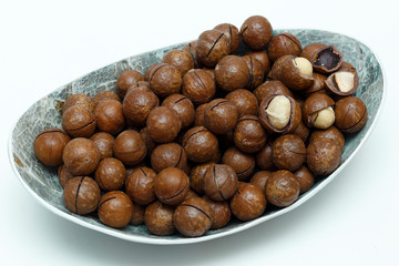 Macadamia nuts in silver bowl on white background top view