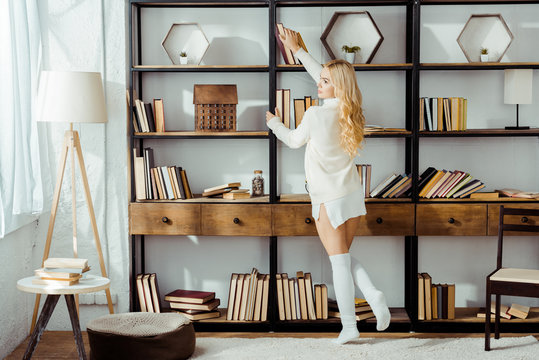 beautiful adult woman taking book from wooden rack
