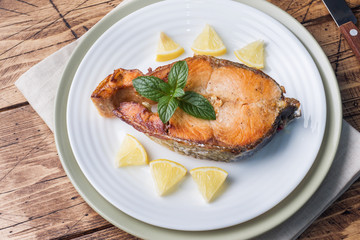 Steak baked fish salmon on a plate with lemon. Wooden table.