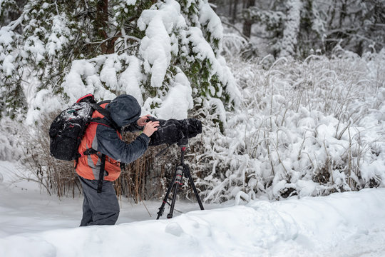 Behind the scene. Cameraman with video camera on tripod, shooting the film scene at outdoor location, on nature, forest, cold winter snowy day