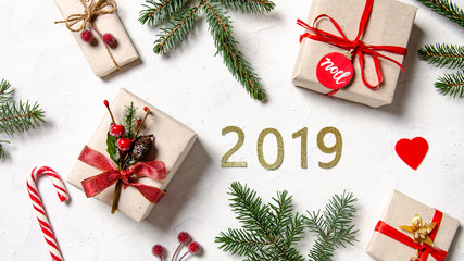 Fototapeta na wymiar New year's background 2019 with homemade wrapped in craft paper presents, candy cane and fir branches on white surface. Top view