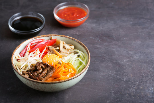 Traditional Asian Bibimbap dish with rice and vegetables on dark background with copy space