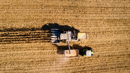 Fototapeta na wymiar Aerial view of combine harvester unloading corn in tractor trailer