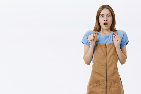 Portrait of stunned afriad girl gasping from shocked and worried feeling remaining speechless pressing hands to chest from nervousness and astonishment standing impressed and concerned over gray wall