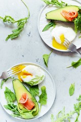 Breakfast on a plate with poached egg with avocado, arugula and salted salmon on a gray background