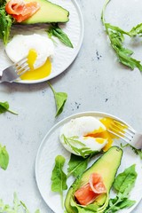 Breakfast on a plate with poached egg with avocado, arugula and salted salmon on a gray background
