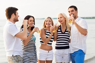 friendship, summer holidays and people concept - group of happy friends in striped clothes drinking non alcoholic beer on beach