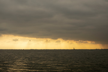 Sailing boat silhouette in front of the skyline of Amsterdam in Holland while the sun is going down and a large cloudy sky.