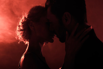 Attractive young couple almost kissing on red smoke background