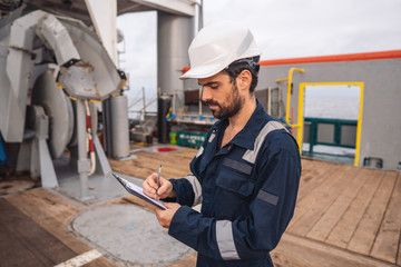 Marine Deck Officer or Chief mate on deck of vessel or ship . He is inspecting and writing...