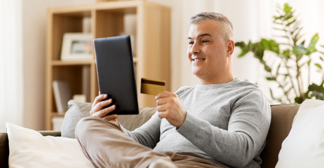 technology, online shopping, people and lifestyle concept - man with tablet pc computer and credit card sitting on sofa at home