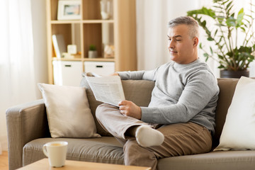 leisure, information, people and mass media concept - man reading newspaper at home