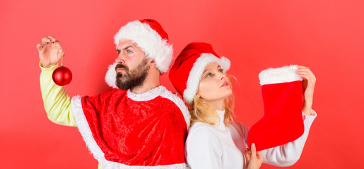 Christmas stocking tradition. Woman and bearded man in santa hat waiting christmas red background. Couple christmas santa costume hold sock and ornament ball. Christmas celebration concept