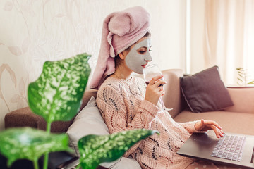 Young woman with facial mask applied drinking wine while using laptop on couch. Relaxing at home