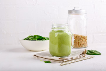 Green smoothie drink in glass jar on white. Mixed cocktail with spinach and green buckwheat.