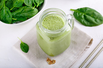 Green smoothie drink in glass jar on white. Mixed cocktail with spinach and green buckwheat.
