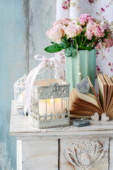 Vintage birdcage with cande and bouquet of pink roses in ceramic vase.