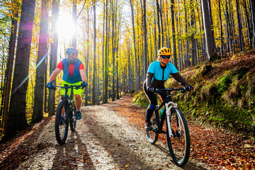 Naklejka premium Cycling woman and man at Beskidy mountains autumn forest landscape. Couple riding MTB enduro track. Outdoor sport activity.