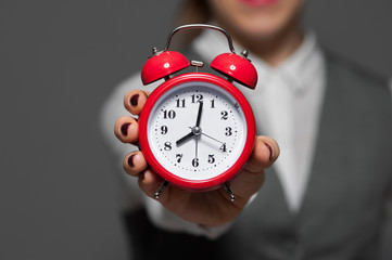 Close-up of red alarm clock in a female hand manicured burgundy nails blurred businesswoman on the grey background