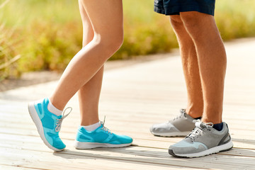 fitness, sport and footwear concept - legs of couple of sportsmen in sneakers outdoors