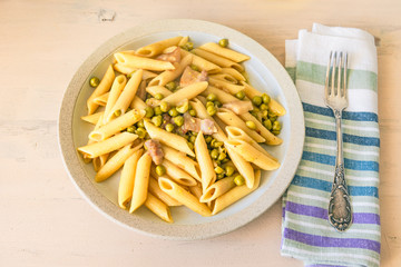 Pasta with peas and pancetta on a plate on a light wooden table