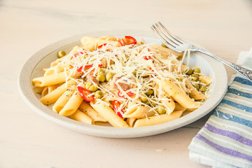 Italian cuisine - Pasta with peas and bacon with parmesan cheese on a plate on a light wooden table