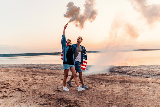american couple walking along the beach and holding hand flare or fusee covered in american flag. Freedom and independence concept