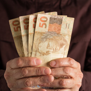 Brazilian currency: Real. Front view senior person holding bills.