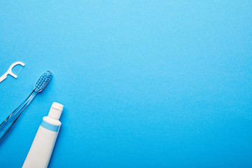 top view of dental floss, toothbrush and toothpaste arranged on blue backdrop, dentistry concept