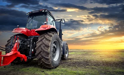 Foto op Plexiglas Tractor Landbouwtractor die in het veld werkt bij zonsondergang op de achtergrond