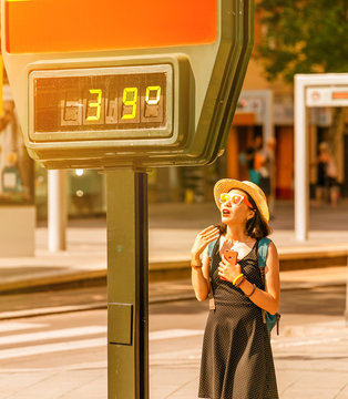 Woman Suffers From Heat And Sunstroke Outside In Hot Weather On The Background Of A Street Thermometer Showing 39 Degrees Celsius