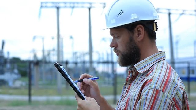 Station technical director with working drawings at nuclear power station. Worker in white helmet with engineering drawing near outdoor switchgear at nuclear power station